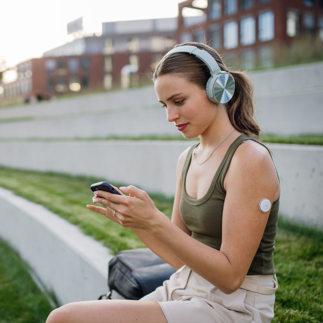 Someone sitting down checking their phone with a CGM sensor on their arm